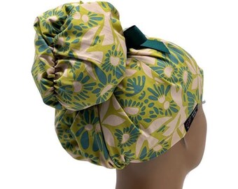Könnte beinhalten: Eine OP-Haube mit einem floralen Muster in Limettengrün, Petrol und Creme. Die Haube verfügt über eine geraffte Tasche für einen Dutt am Hinterkopf, die mit einem dunkelgrünen Band gebunden ist, sowie ein kleines schwarzes Stoffetikett an der Seite.