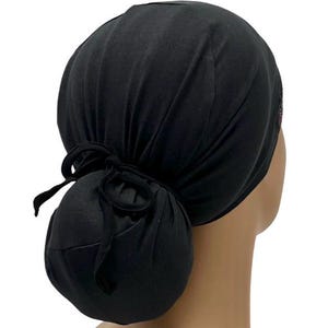 May include: Black scrub hat with a bun cover and a tie at the back. The hat is made of a soft, stretchy fabric.