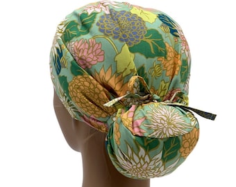 Puede incluir: Un gorro de quirófano de color verde, rosa y amarillo con estampado floral y un agujero para la coleta. El gorro está atado en la parte posterior con un lazo.