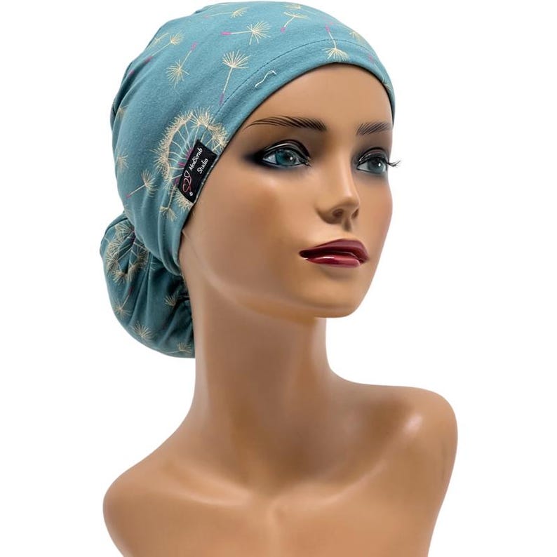Peut inclure: Bonnet de gommage bleu sarcelle avec un motif de pissenlit. Le bonnet est en tissu doux et pr&eacute;sente un design en queue de cheval. Il y a une petite &eacute;tiquette noire avec le texte "MedSock Studio".
