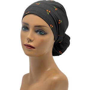 May include: Black scrub hat with a cherry print. The hat is tied at the back of the head.