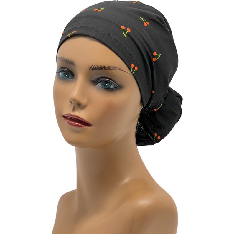 May include: Black scrub hat with a cherry print. The hat is tied at the back of the head.