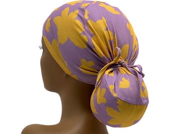 May include: Purple and yellow patterned surgical scrub hat with a ponytail hole. The hat is tied at the back to create a bun.