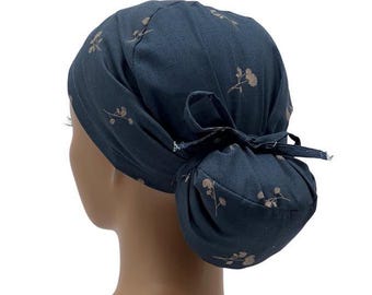 Könnte beinhalten: Eine dunkelblaue OP-Mütze mit einem Pferdeschwanzloch und einem floralen Muster in hellbrauner Farbe.