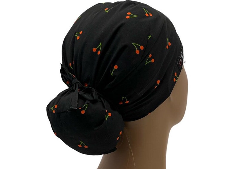 May include: Black scrub hat with a cherry print. The hat has a bun covering in the back.