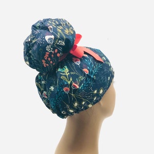 May include: A dark blue scrub hat with a floral print and a red ribbon. The hat has a bun-shaped top and is designed for medical professionals.