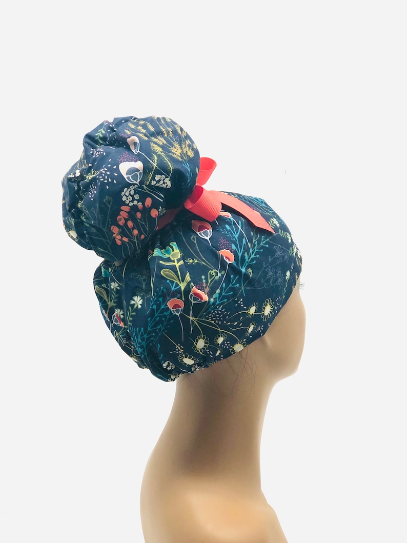 May include: A dark blue scrub hat with a floral print and a red ribbon. The hat has a bun-shaped top and is designed for medical professionals.