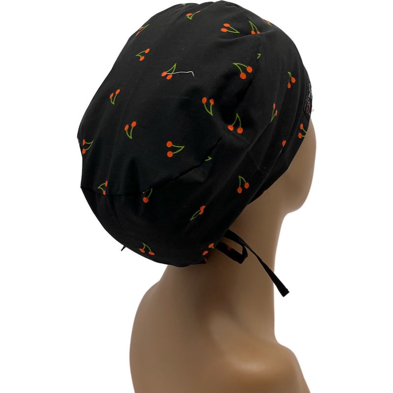 May include: Black scrub hat with a cherry print. The hat has a tie at the back.