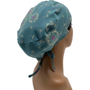 Peut inclure: Bonnet chirurgical bleu sarcelle avec un motif de pissenlits. Le bonnet pr&eacute;sente un motif r&eacute;p&eacute;t&eacute; de t&ecirc;tes de graines de pissenlits blanches avec des centres roses. Le bonnet a des liens &agrave; l'arri&egrave;re pour un ajustement r&eacute;glable.