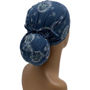Pode incluir: Uma touca cir&uacute;rgica azul marinho com um padr&atilde;o de dente-de-le&atilde;o branco. A touca &eacute; amarrada em um coque na parte de tr&aacute;s com uma gravata de tecido combinando. As flores de dente-de-le&atilde;o t&ecirc;m um centro verde.