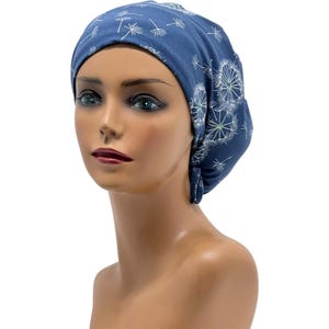 Pode incluir: Um gorro de tecido azul com um padr&atilde;o de dente-de-le&atilde;o. O gorro &eacute; feito de material macio e foi projetado para cobrir a cabe&ccedil;a. O desenho do dente-de-le&atilde;o &eacute; branco e verde claro, criando um contraste com o fundo azul.