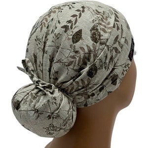May include: A beige scrub hat with a brown leaf pattern. The hat is tied in a bun at the back.