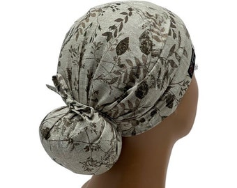 May include: A beige scrub hat with a brown leaf pattern. The hat is tied in a bun at the back.