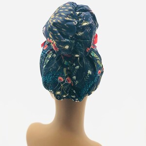 May include: A dark blue satin bun cover with a floral print in shades of red, green, and yellow. The bun cover has a red ribbon tied around it.
