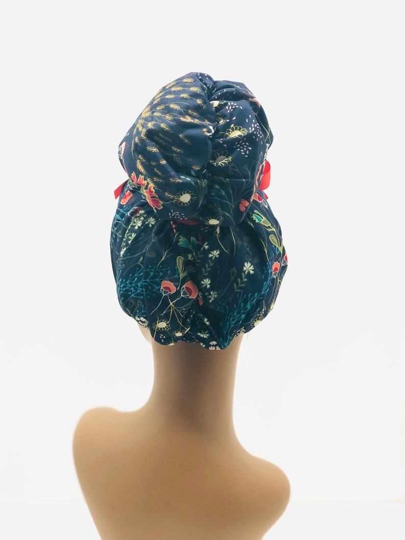 May include: A dark blue satin bun cover with a floral print in shades of red, green, and yellow. The bun cover has a red ribbon tied around it.