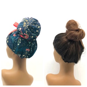 May include: Two mannequins, one wearing a blue and floral print fabric bun cover with a red ribbon, and the other with a brown bun hairstyle.