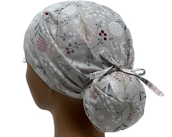May include: A gray scrub cap with a floral pattern featuring white, pink, and burgundy flowers and green leaves. The cap has a gathered back and a tie closure. The fabric is a soft, light material.