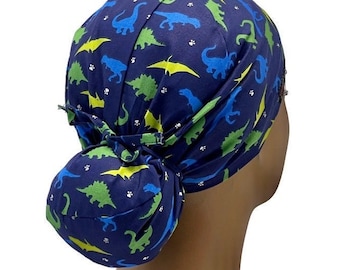 Könnte beinhalten: Eine blaue OP-Mütze mit Dinosaurier-Druck. Die Mütze ist hinten zu einem Dutt gebunden.