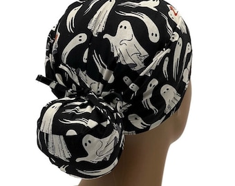 May include: Black scrub hat with a white ghost pattern. The hat has a bun tie in the back.