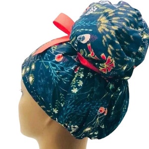 May include: A blue and green floral print surgical scrub hat with a red bow. The hat is designed to be worn with a bun.