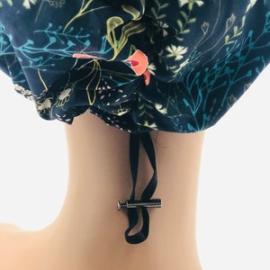 May include: A blue and white floral print surgical scrub hat with a black drawstring and a silver toggle. The hat is made of a soft, comfortable fabric and is designed to keep hair out of the way during surgery.