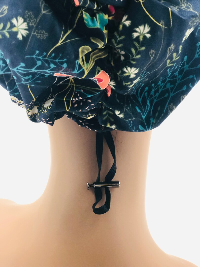 May include: A blue and white floral print surgical scrub hat with a black drawstring and a silver toggle. The hat is made of a soft, comfortable fabric and is designed to keep hair out of the way during surgery.
