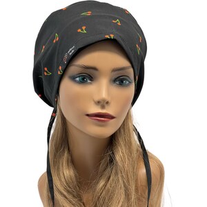 May include: Black surgical scrub hat with a cherry print. The hat has two long ties that can be tied at the back of the neck.