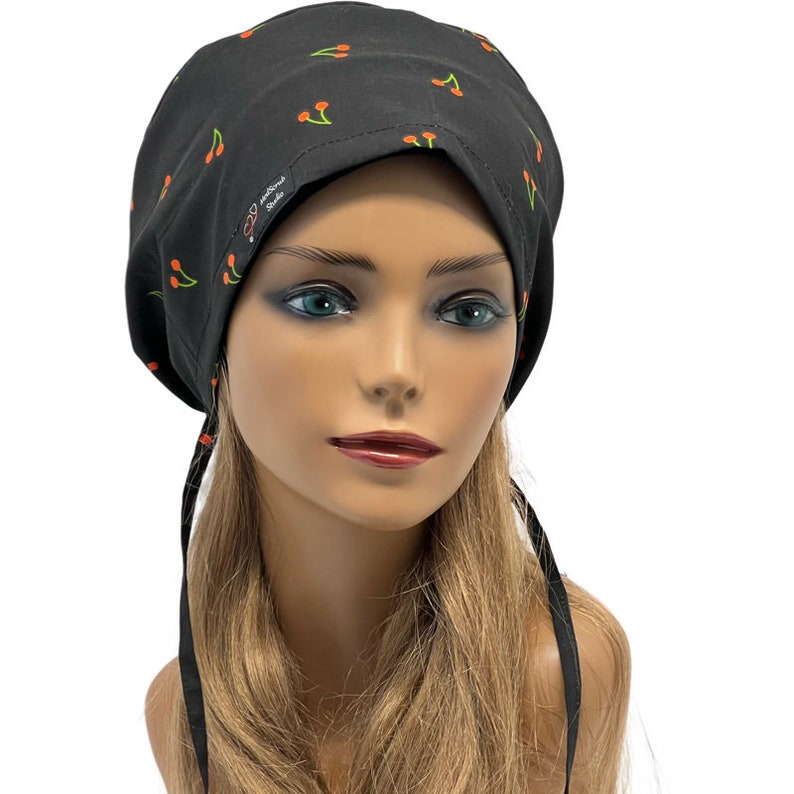 May include: Black surgical scrub hat with a cherry print. The hat has two long ties that can be tied at the back of the neck.