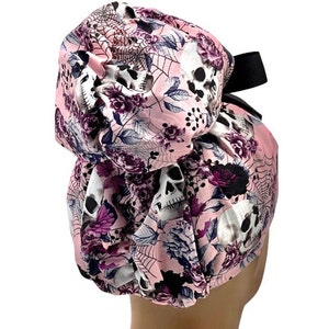 May include: Pink surgical scrub hat with a skull and floral print. The hat has a black elastic band.