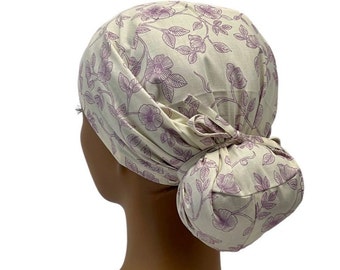 Puede incluir: Un gorro de quirófano blanco con un estampado floral morado. El gorro tiene un lazo para el moño y está hecho de una tela suave y cómoda.