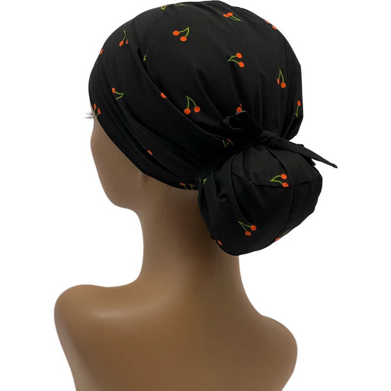 May include: Black scrub hat with a cherry print. The hat has a bun covering and a tie at the back.