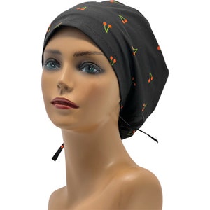 May include: Black scrub hat with a cherry print. The hat has a tie at the back.