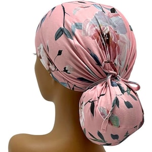 May include: Pink surgical scrub hat with a floral print featuring pink, white, and blue flowers and leaves. The hat is tied in a bun at the back.