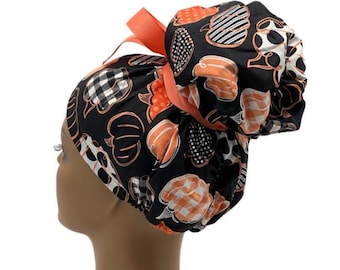 Könnte beinhalten: Eine schwarze OP-Haube mit einem wiederkehrenden Muster aus orangefarbenen und weißen Kürbissen in verschiedenen Texturen wie Karos und Punkten. Die Haube verfügt über eine geraffte Tasche am Hinterkopf, die mit einem orangefarbenen Band gebunden ist.