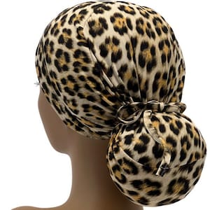 May include: A leopard print surgical scrub hat with a bun. The hat is tied at the back with a bow.