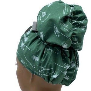 May include: Green satin hair bonnet with a white floral pattern. The bonnet is gathered at the top to create a bun shape.