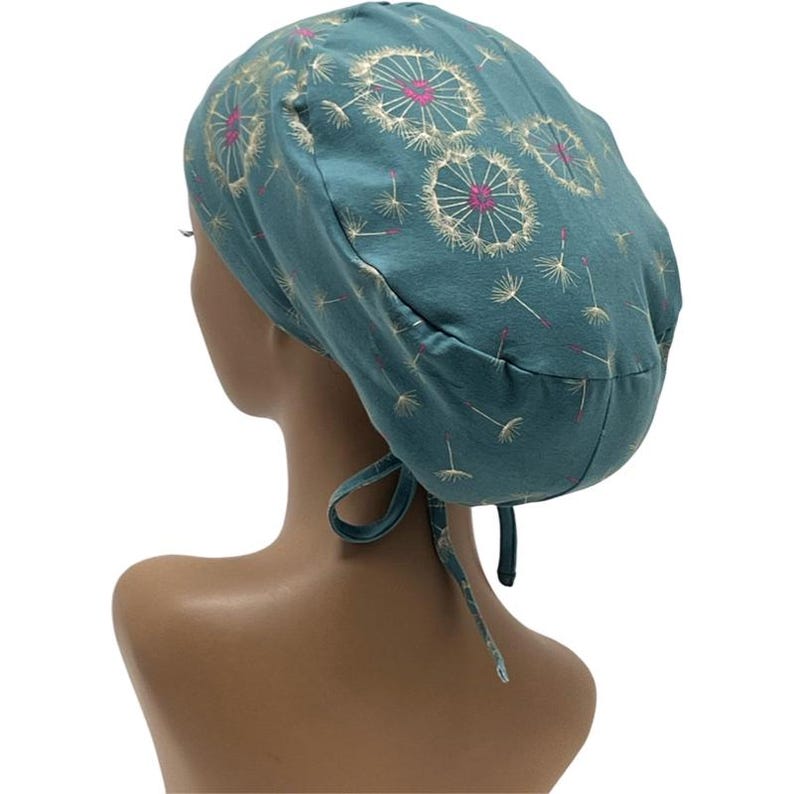 Peut inclure: Bonnet de chirurgien de couleur teal, orn&eacute; d'un motif de pissenlits blancs et roses. Le bonnet est nou&eacute; &agrave; l'arri&egrave;re avec des liens en tissu assortis. Con&ccedil;u pour les professionnels de la sant&eacute;.
