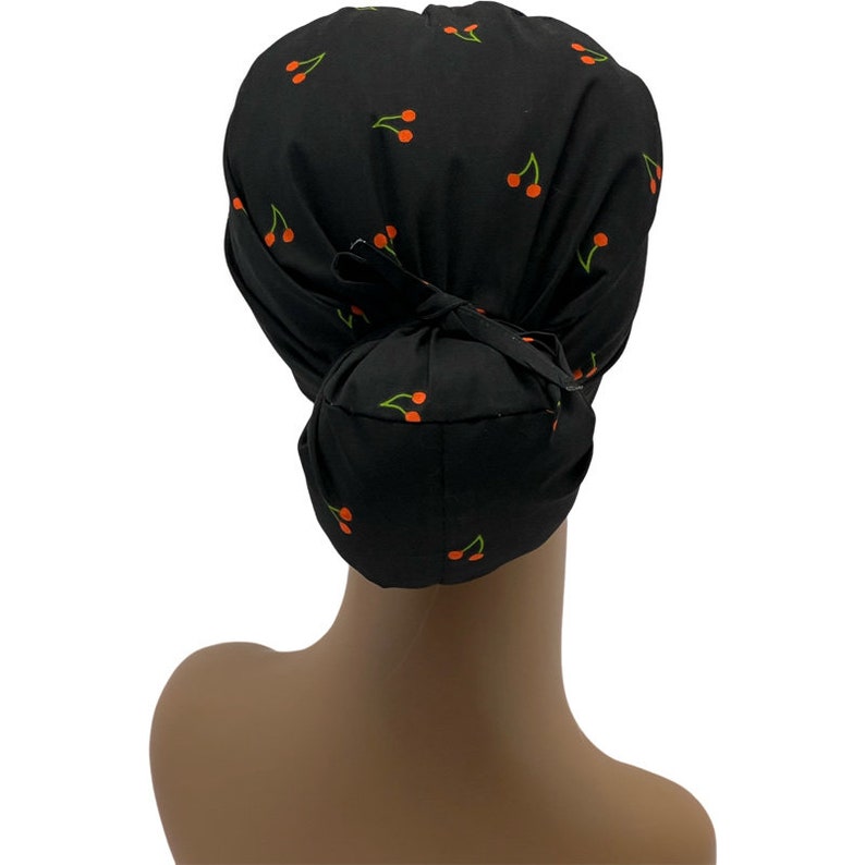 May include: Black scrub hat with a cherry print. The hat has a ponytail opening in the back and ties at the top.