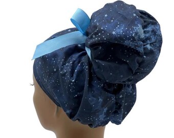 Könnte beinhalten: Eine dunkelblaue OP-Haube mit einem weißen Sternenmuster auf dem Stoff. Die Haube hat einen gerafften, voluminösen hinteren Bereich, der für Haare ausgelegt ist, und ist mit einem hellblauen Band verziert, das oben zu einer Schleife gebunden ist.