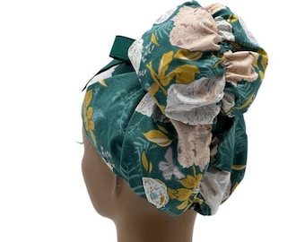 Könnte beinhalten: Ein dunkelgrünes Haaraccessoire aus Stoff mit einem Blumenmuster aus hellrosa Blüten und senfgelben Blättern. Das Accessoire hat ein gerafftes, voluminöses Design mit einem Gummiband, das eine Dutt-Form auf einem Schaufensterpuppenkopf bildet.