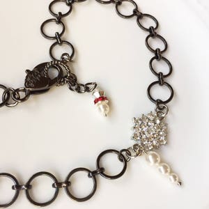 Op de afbeelding: Een zwarte ketting met een hartvormige sluiting, een sneeuwvlok-hanger met strass en een witte parel hanger.