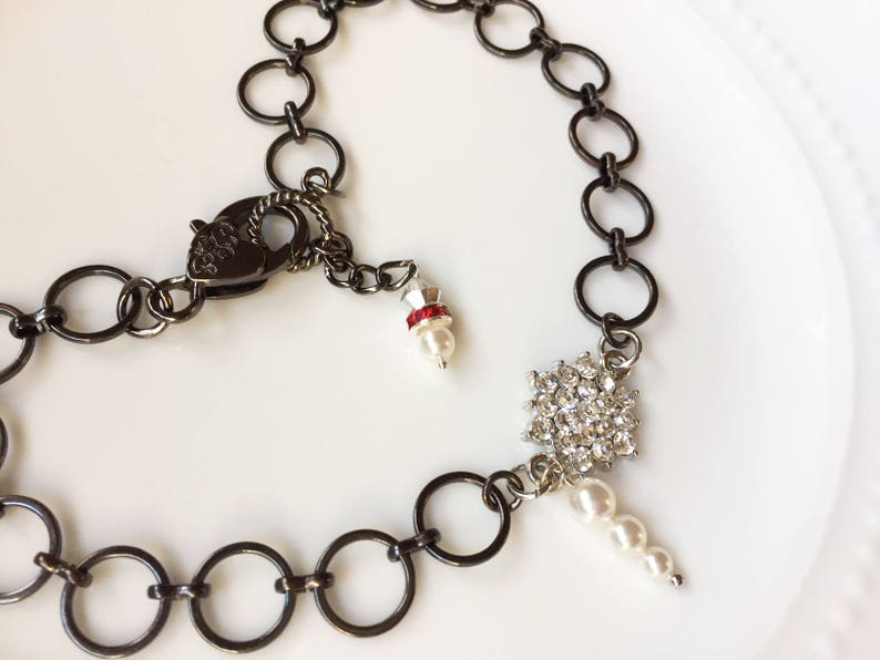 Op de afbeelding: Een zwarte ketting met een hartvormige sluiting, een sneeuwvlok-hanger met strass en een witte parel hanger.