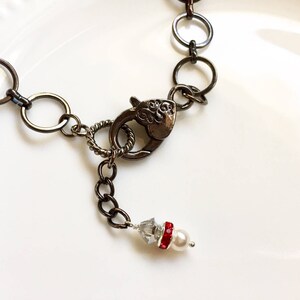 Op de afbeelding: Een zilveren ketting met een karabijn sluiting en een klein parel en rode strass accent.