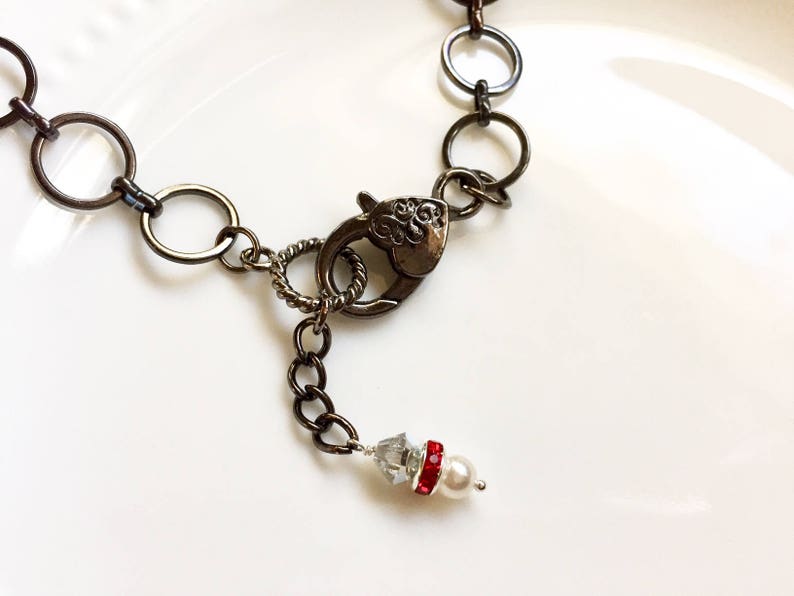 Op de afbeelding: Een zilveren ketting met een karabijn sluiting en een klein parel en rode strass accent.