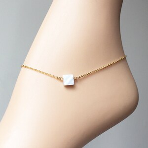 May include: A delicate gold chain anklet with a white square charm.