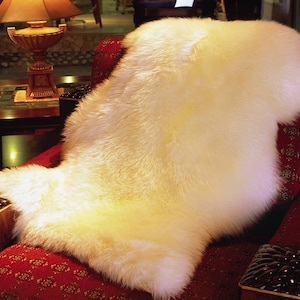 May include: A white sheepskin rug is draped over a red armchair with floral upholstery. The rug is soft and fluffy, and the armchair is ornate with dark wood accents.