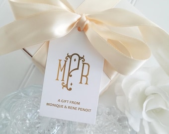May include: A white gift tag with a gold monogram "MPR" and the text "A gift from Monique & Rene Penoit". The tag is tied with a cream satin ribbon.