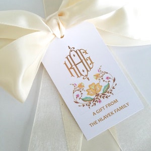 May include: A white gift tag with a gold monogram "HHG" and a floral design. The tag reads "A gift from the Hlavek family".