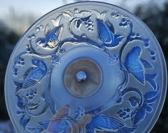 Puede incluir: Un plato decorativo redondo de vidrio transparente con un diseño en relieve de pájaros azules y follaje. El plato tiene una hendidura central circular con una fijación metálica. Los pájaros están detallados con acentos azules.