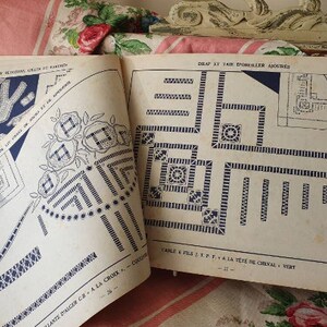 Peut inclure: Un livre de mod&egrave;les de point de croix vintage avec des instructions pour cr&eacute;er une housse de coussin. Le livre pr&eacute;sente un motif bleu et blanc avec un motif floral et un motif g&eacute;om&eacute;trique. Le texte sur la page indique "Drap ST. KT TAIK D'OREILLER AJOURES" et "CABLE & FILS T.P.F. A LA T&Ecirc;TE DE CHEVAL - VERT".